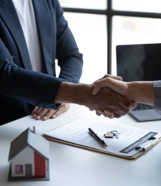 Two young Asian businessmen shake hands after signing a contract to invest in a village project. real estate, with businesswomen joining in showing joy and clapping in the office.